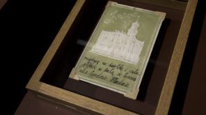 Fotografia barwna. Zielona pocztówka z wytłoczonym białym wizerunkiem ratusza w Jarosławiu. W dolnej części pocztówki odręczna korespondencja.